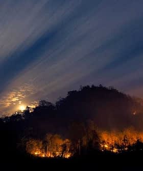 A mountain landscape with visible flames and smoke under a night sky with clouds and a full moon. - Olive Oil Times