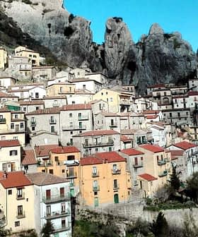 A hillside village featuring colorful houses with red roofs against rocky mountains. - Olive Oil Times