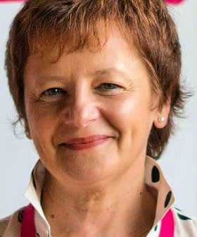 Woman with short brown hair wearing a polka dot blouse and smiling at the camera. - Olive Oil Times