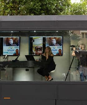 Two individuals participating in a video conference with screens displaying images in a modern setting. - Olive Oil Times