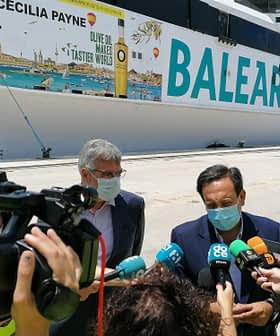 Two men speaking during a press conference in front of a Balearia ferry with promotional graphics. - Olive Oil Times