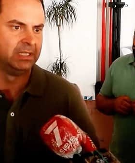 A man in a green shirt speaking to reporters with a microphone in front of him. - Olive Oil Times