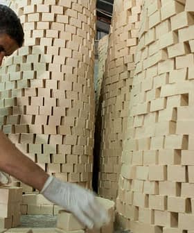 A man wearing gloves stacking rectangular soap blocks in a workshop environment. - Olive Oil Times