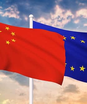 Chinese flag on the left and European Union flag on the right, both waving against a cloudy sky. - Olive Oil Times