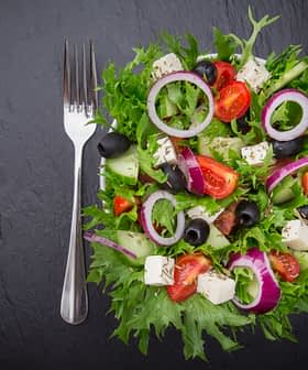 A colorful garden salad featuring mixed greens, tomatoes, cucumbers, olives, and feta cheese on a dark surface. - Olive Oil Times