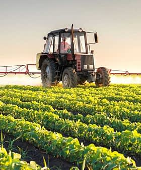 A tractor spraying crops in a field with rows of green plants under a clear sky. - Olive Oil Times