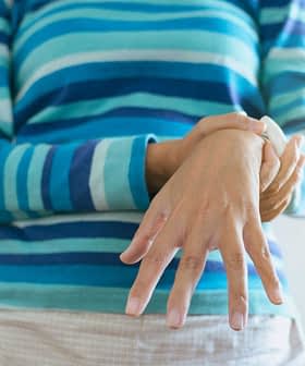 Individual wearing a striped sweater, holding their wrist with one hand while standing indoors. - Olive Oil Times