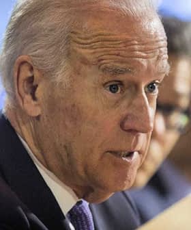 A man in a suit speaking during a conference, holding a document in his hand. - Olive Oil Times