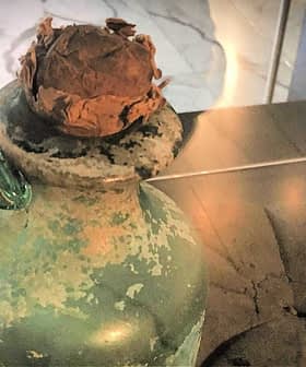 An ancient green glass jug with a cork stopper displayed on a surface. - Olive Oil Times