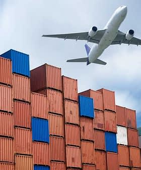 An airplane flying above a stack of colorful shipping containers at a port. - Olive Oil Times