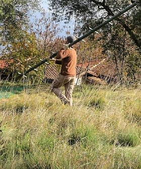 Individual holding a long pole while standing in a grassy field with trees in the background. - Olive Oil Times