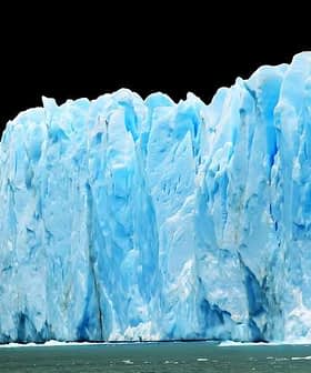 A large glacier with blue ice formations and a jagged edge against a dark background. - Olive Oil Times