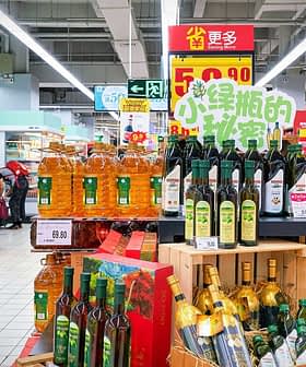 Shelves filled with different brands of cooking oils in a supermarket aisle. - Olive Oil Times