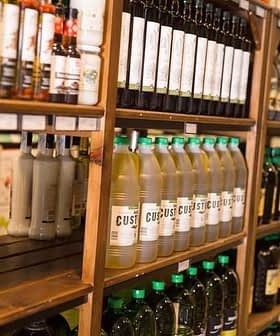 Shelves displaying various bottles of oils and condiments in a store setting. - Olive Oil Times