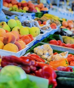 A selection of fresh fruits and vegetables displayed at a market stall, including peaches, carrots, and cucumbers. - Olive Oil Times