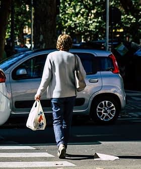 Individual walking on a street while carrying a grocery bag in one hand. - Olive Oil Times
