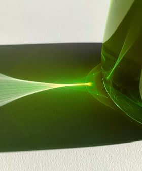 Green glass bottle casting a light reflection on a white surface. - Olive Oil Times