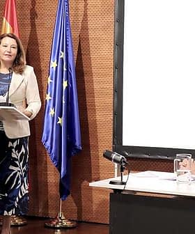 A woman presenting at a podium with flags of Spain and the European Union in the background. - Olive Oil Times