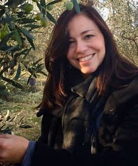 Woman smiling while picking olives from an olive tree in an outdoor setting. - Olive Oil Times