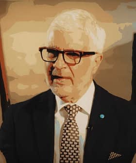 A man with white hair and glasses speaking, wearing a dark suit and patterned tie. - Olive Oil Times