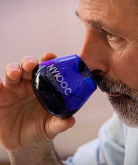 Man with a beard holding a blue glass for tasting olive oil, bringing it close to his nose. - Olive Oil Times