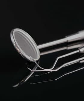 Set of dental examination instruments including a mirror and explorer on a reflective surface. - Olive Oil Times