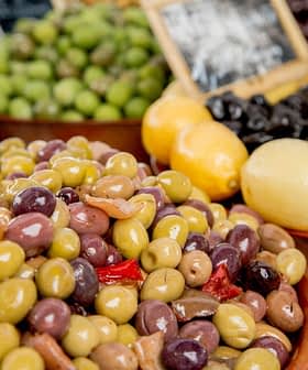 A bowl filled with various types of olives alongside lemons at a market display. - Olive Oil Times