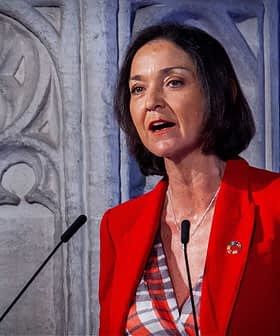 Woman in a red blazer speaking at a podium with a decorative background. - Olive Oil Times