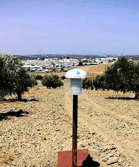 Monitoring device positioned in an olive grove with trees in the background. - Olive Oil Times