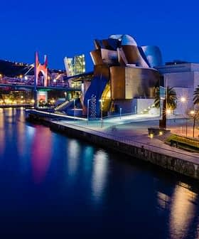 Guggenheim Museum in Bilbao illuminated at night with reflections in the water. - Olive Oil Times