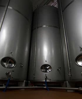 Three stainless steel storage tanks with valves and pipes in a facility. - Olive Oil Times