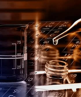 A beaker with liquid next to a pipette and glass vials on a periodic table background. - Olive Oil Times