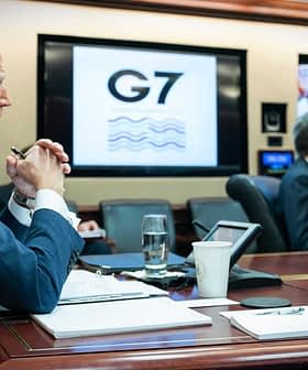Joe Biden seated at a conference table during a G7 meeting with screens displaying participants. - Olive Oil Times