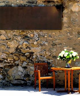 A wooden table with two chairs and a vase of flowers on a stone wall background. - Olive Oil Times