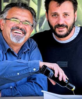 Two men smiling while one pours olive oil from a bottle into a dish. - Olive Oil Times