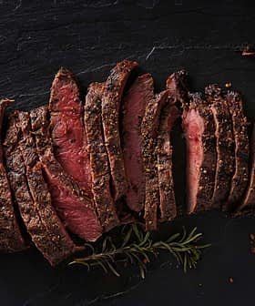 Sliced roast beef arranged on a slate surface with herbs. - Olive Oil Times