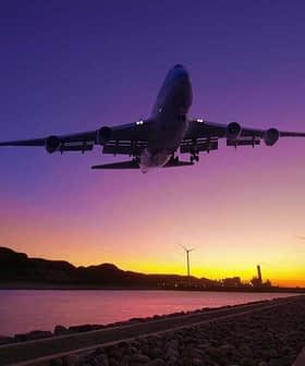 An airplane flying above a river during sunset with wind turbines in the background. - Olive Oil Times