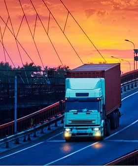 A white truck with a container driving on a bridge during sunset with colorful sky. - Olive Oil Times