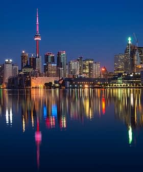 Toronto city skyline featuring the CN Tower and illuminated buildings reflected in water at night. - Olive Oil Times