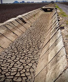 Cracked dry irrigation canal running alongside a gravel road in an agricultural area. - Olive Oil Times