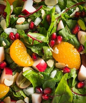 A bowl of mixed green salad featuring spinach, apple pieces, orange segments, pomegranate seeds, and sliced almonds. - Olive Oil Times
