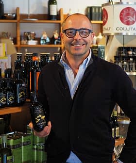 Man with glasses holding a bottle of olive oil in a store filled with various oil products. - Olive Oil Times