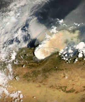 Satellite view showing smoke rising from a wildfire in a landscape with clouds and terrain visible. - Olive Oil Times