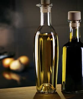 Two glass bottles containing olive oil, one with a light golden liquid and the other with a dark liquid, placed on a wooden surface. - Olive Oil Times