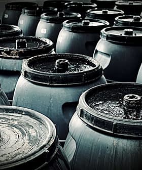A group of dark storage barrels arranged closely together, showing their tops and lids. - Olive Oil Times