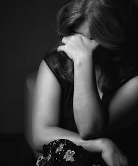 A woman with long hair sitting with her hand covering her face in a black and white photograph. - Olive Oil Times