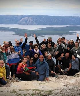 A large group of people posing together on a mountain with arms raised in celebration. - Olive Oil Times