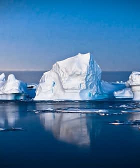 Icebergs floating in calm waters with a blue sky in the background during twilight. - Olive Oil Times