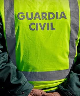A Guardia Civil officer wearing a high-visibility vest stands with hands behind back on a roadside. - Olive Oil Times