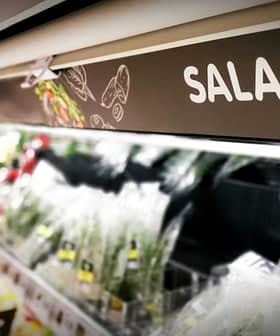 Sign labeled 'SALAD' in a grocery store aisle with various salad ingredients visible. - Olive Oil Times